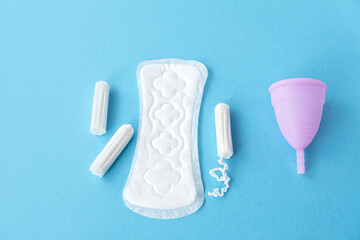 Menstrual cycle. Alternative means of hygiene and protection in critical days for women. Sanitary pads, tampons and silicone menstrual cup on blue background. Selective focus. Copy space