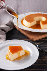 .Delicious condensed milk pudding on white plate. Someone pouring caramel sauce.