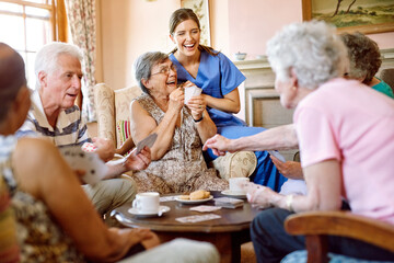 The suspense keeps the game exciting. Shot of a group of happy seniors playing a card game in their retirement home while a nurse watches. - Powered by Adobe