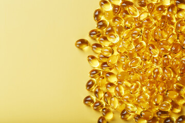 Pile of golden capsules of vitamin D3 on a yellow background with free space