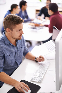 Modern business is fast-paced innovative and online. Shot of a young designer working at his computer with colleagues in the background.