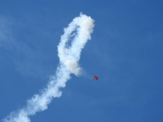 A red biplane performing aerobatic stunts at an airshow in the skies of southern California.