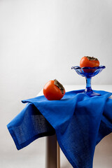 Still life with persimmon, glass vase and blue fabric. Vertical orientation, copy space.