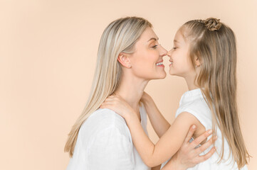 Obraz na płótnie Canvas Mom and little daughter on a beige background in white clothes. Nose to nose.