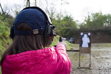 A young attractive woman pointing a gun at the target on shooting range, selective focus on the target