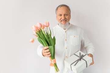 Portrait of an attractive old man with flowers and a gift. A gray-haired man with a beard with tulips on a beige background.