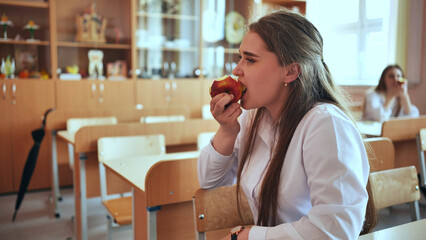 Schoolgirl eat apple in class during recess.