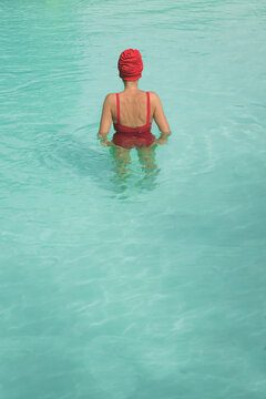 Woman in red swim suit and bathing cap seen in swimming pool in summer