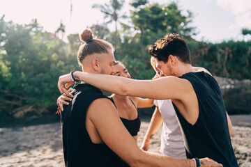 Young hipster guys enjoying weekend vibes at seashore coastline talking about summer yoga tour vacations in Indonesia, male and female friends in sportive clothes discussing team building outdoors