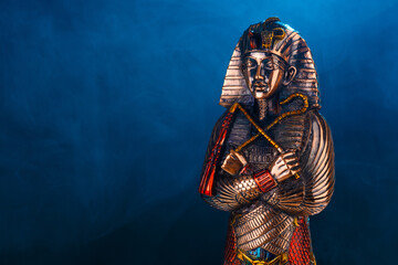 golden Egyptian pharaoh figurine in blue smoke on a black background.