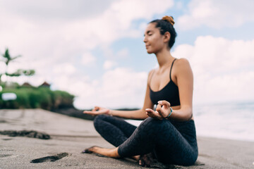 Fototapeta na wymiar Harmony and meditation training during morning yoga at coastline beach, blurred female in sportswear sitting in lotus pose during aerobic pilates for exercising own body concentration in asana