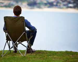 The perfect place to enjoy the scenery. Rear-view of a young man sitting on a camping chair and...