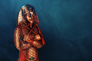 golden Egyptian pharaoh figurine in blue smoke on a black background.