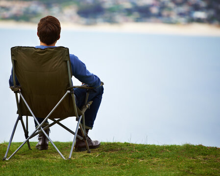 The perfect place to enjoy the scenery. Rear-view of a young man sitting on a camping chair and looking at the view.