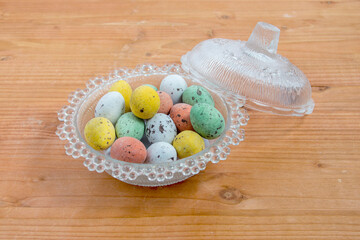 glass candy container with lid and colored easter eggs on wood