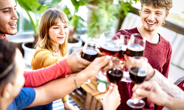 Trendy friends drinking and toasting red wine at rooftop party - Young people having fun together at restaurant winery bar on happy hour - Dining life style concept with bright filter - Focus on woman