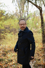 A stylishly dressed man with glasses, a beautiful autumn forest and a river. Elderly Brit.