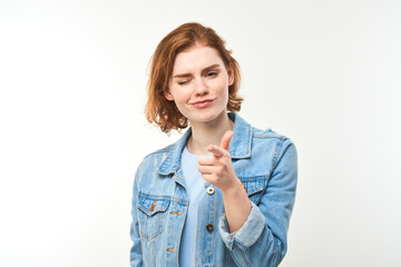 Portrait of friendly redhead girl chooses you, points finger at the camera isolated on white background