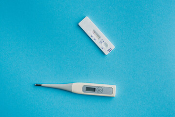 Express test for covid-19 with a positive result and a thermometer on a blue solid background.