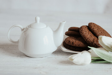 Teapot with tea and flower and chocolate chip cookies, spring still life.
