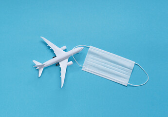 a white plane with a medical mask on a blue background. the concept of social distance. travel planning.