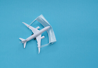 a white plane with a medical mask on a blue background. the concept of social distance. travel planning.
