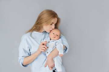 a young mother hugs and kisses her child on a gray background
