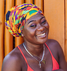 African woman with colorful headdress and a hopeful happy smile stands against a painted wooden wall in the tropical village of Keta Ghana, West Africa