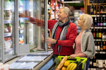 Cheerful senior husband and wife choosing goods in supermarket