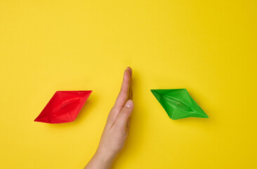 female hand between paper boats on a yellow background, the concept of reconciliation of the...