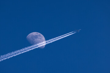 Plane flies pass over the moon on blue sky airplane trail