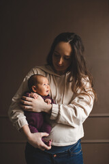 Young mother holding newborn child lying on hands in room at home. Family lifestyle concept. Motherhood.
