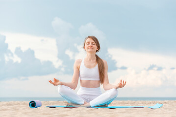 Fototapeta na wymiar Yoga at sunrise on the beach. Young beautiful woman practicing yoga meditation outdoors by the sea