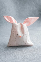 Bag of sweets in shape of Easter bunny with ears on light gray background. Packing made of cotton fabric in form of cute bunny or rabbit, sewing for children, hobby. Vertical Easter card, copy space.