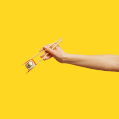 Woman's hand holds sticks sushi roll yellow background