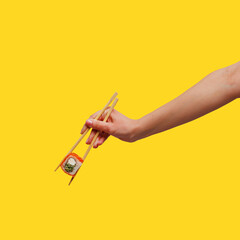 Woman's hand holds sticks sushi roll yellow background
