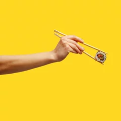 Keuken spatwand met foto Woman's hand holds sticks sushi roll yellow background © Max