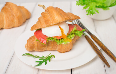Morning breakfast with croissant  salmon lettuce and poached egg. Healthy fish sandwich on white wooden background.