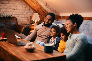 Happy African American family enjoys while watching movie on laptop at home.