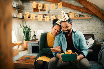 Happy African American man receives Birthday present from his wife at home.