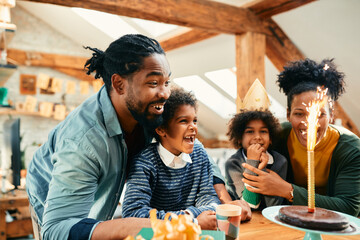 Happy black family has fun while celebrating girl's Birthday with a cake at home.