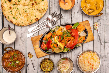 Set of cute Indian food dishes with spicy curry, braised chicken tikka masala, basmati rice, braised lamb curry, spices, cutlery, forks and chili peppers