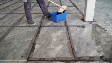 The tiler washes the tiles on the floor after work. A worker cleans large-format ceramic tiles on...