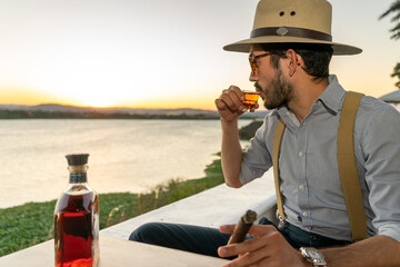 Hipster at bar takes a shot of expensive rum during sunset