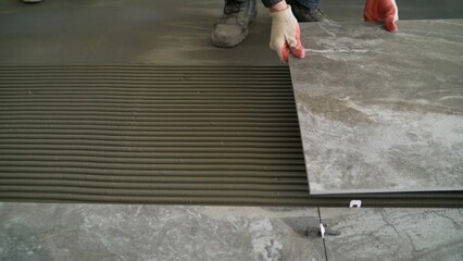 Renovating the floor. Construction workers laying tile over concrete floor using tile levelers,...