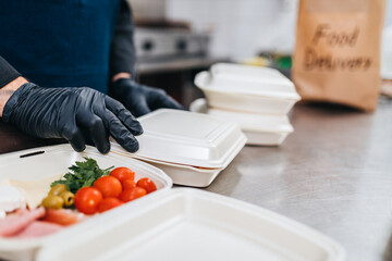 The chef prepares food in the restaurant and packs it in disposable lunch boxes. Food in disposable dishes ready for delivery.