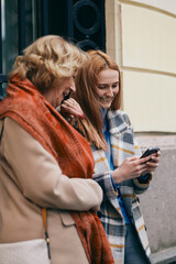A grandmother and her grandchild standing on the street and reading messages on the phone.