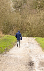 Obraz premium a lone man wearing a hooded top walking along a dirt track in the winter countryside portrait orientation 