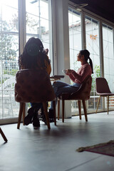 Two multiracial young women sit in a cafe and chat on a coffee break.