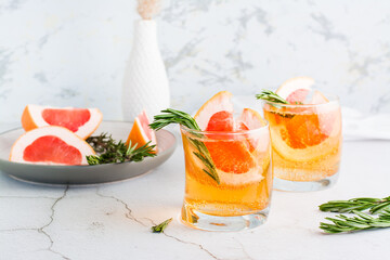 Refreshing grapefruit cocktail with rosemary in glasses and fruit on a plate on the table. Homemade drink.